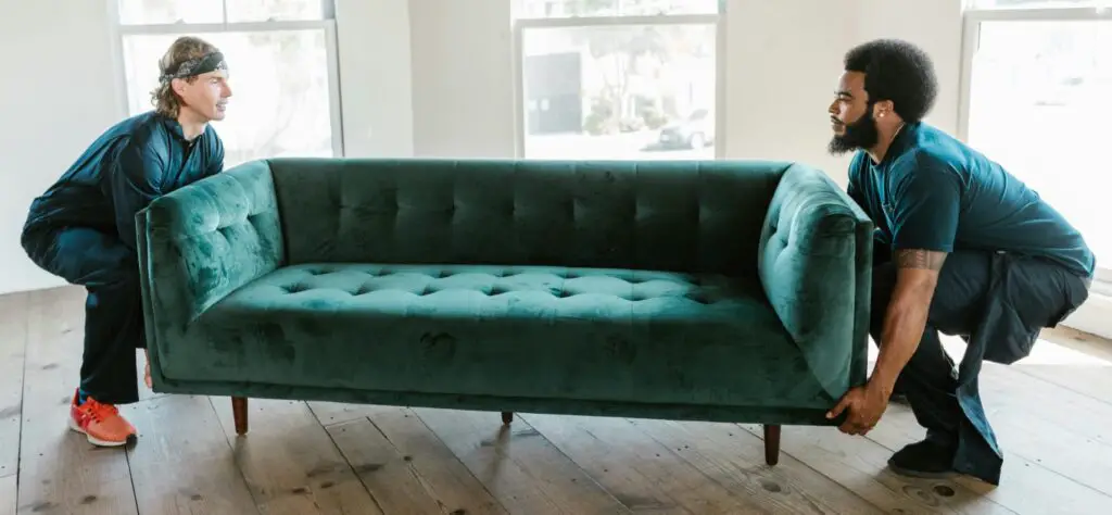 Two people lifting a green sofa